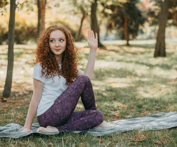 A woman smiling and stretching outdoors in a green park.